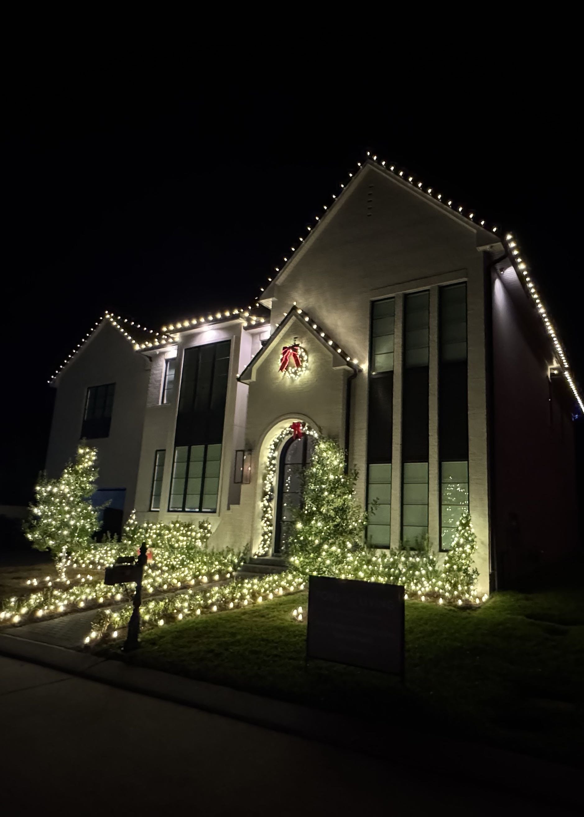 Tall home with warm white roofline, garland and wreath lighting
