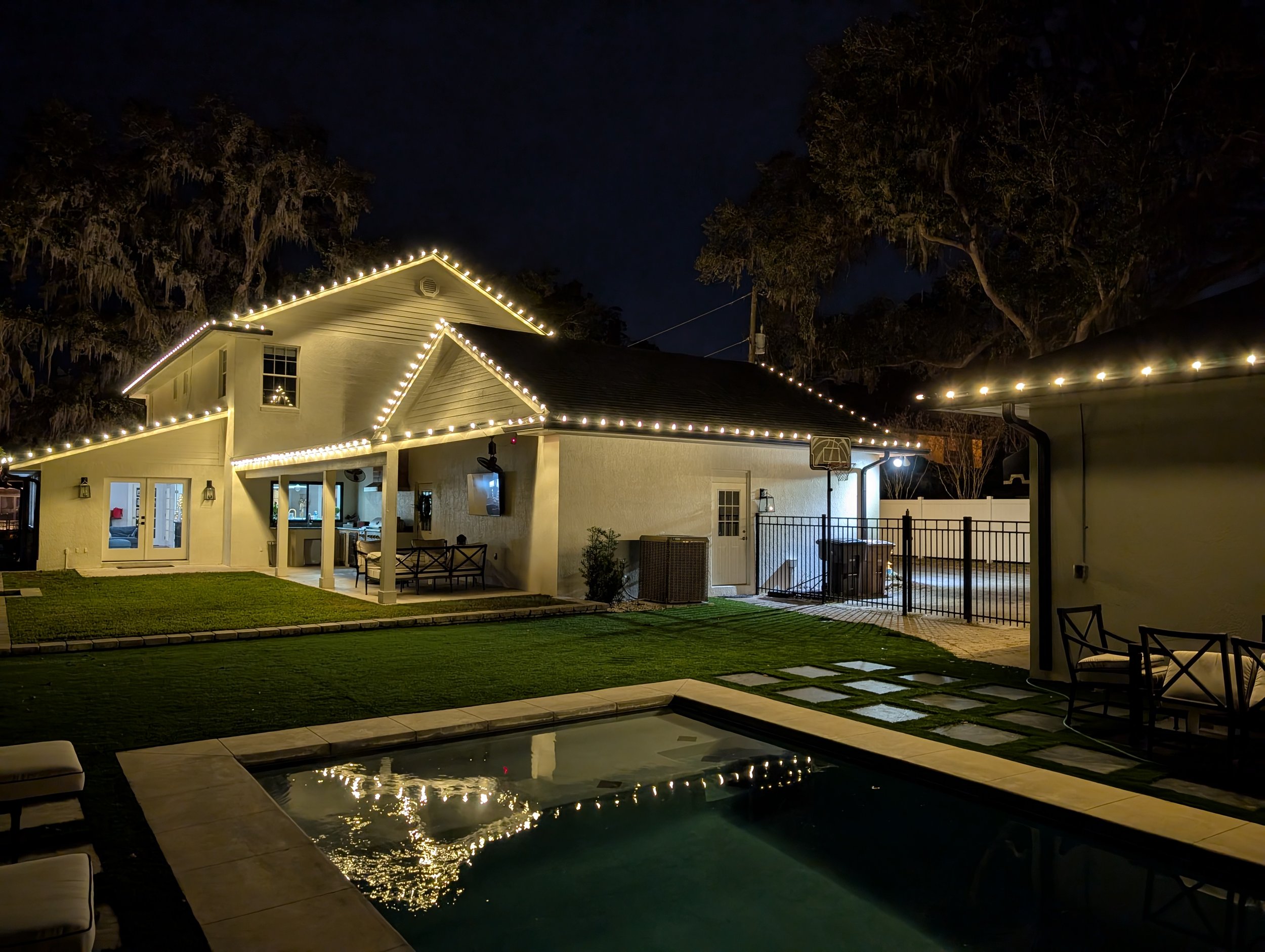 Warm white roofline lighting beside a backyard pool