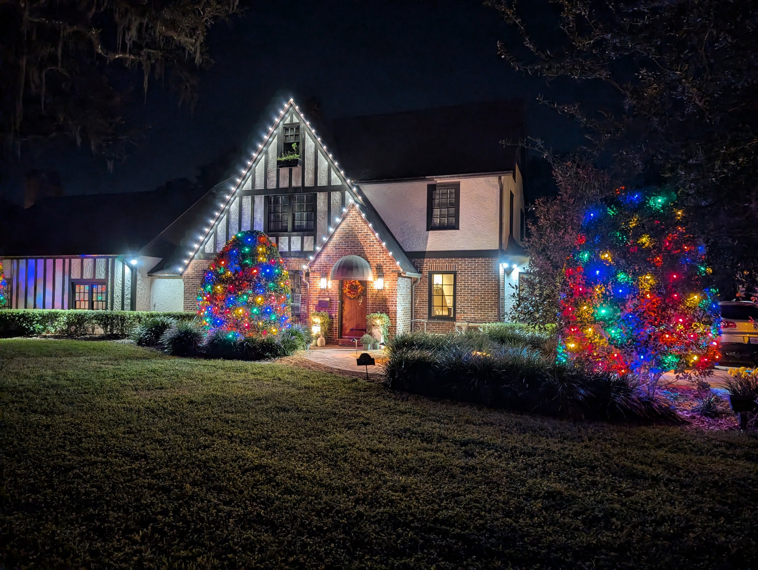 Tudor-style home with white roofline lights and colorful tree lights