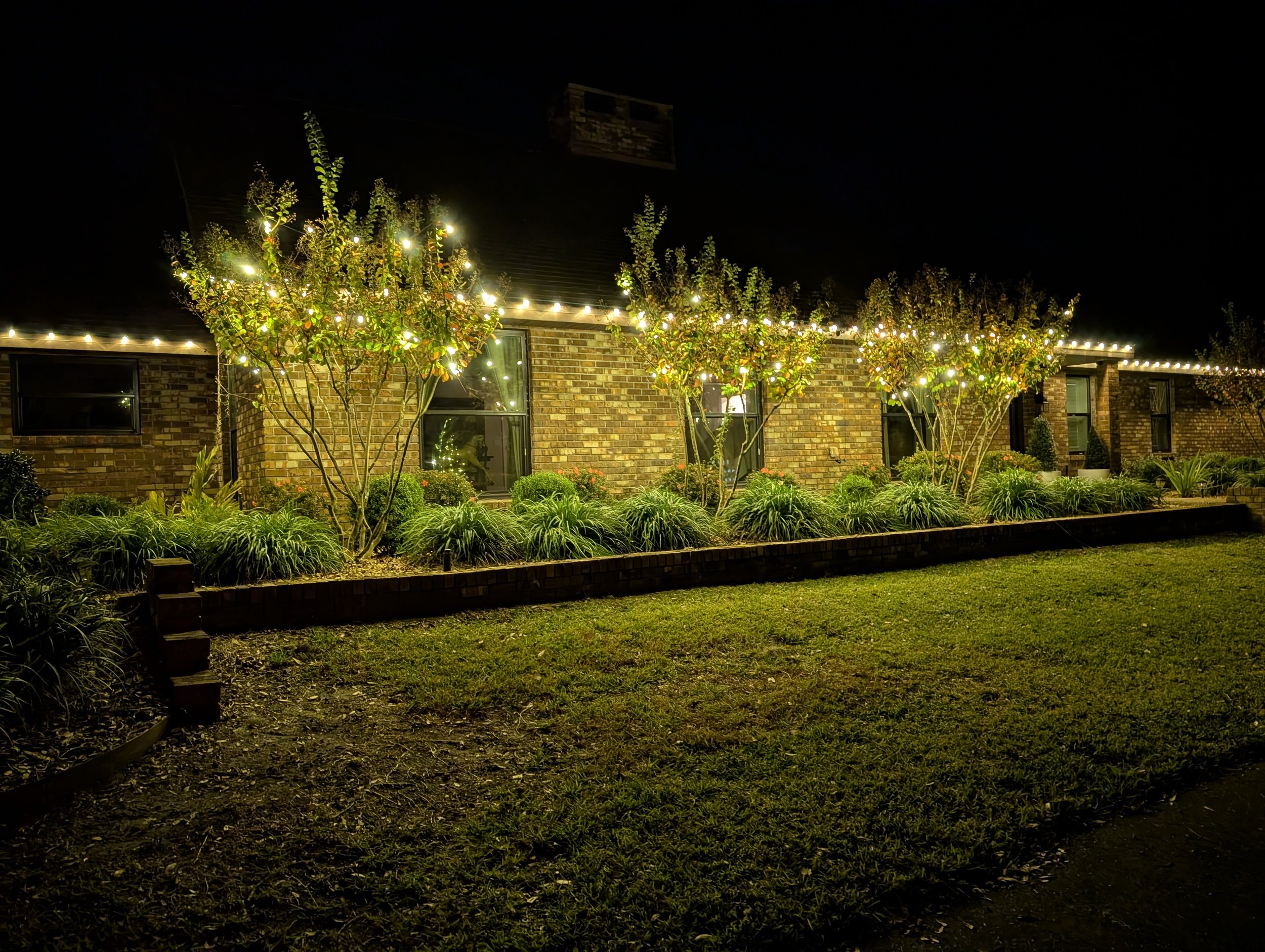 Brick home with warm white roofline and illuminated ornamental trees