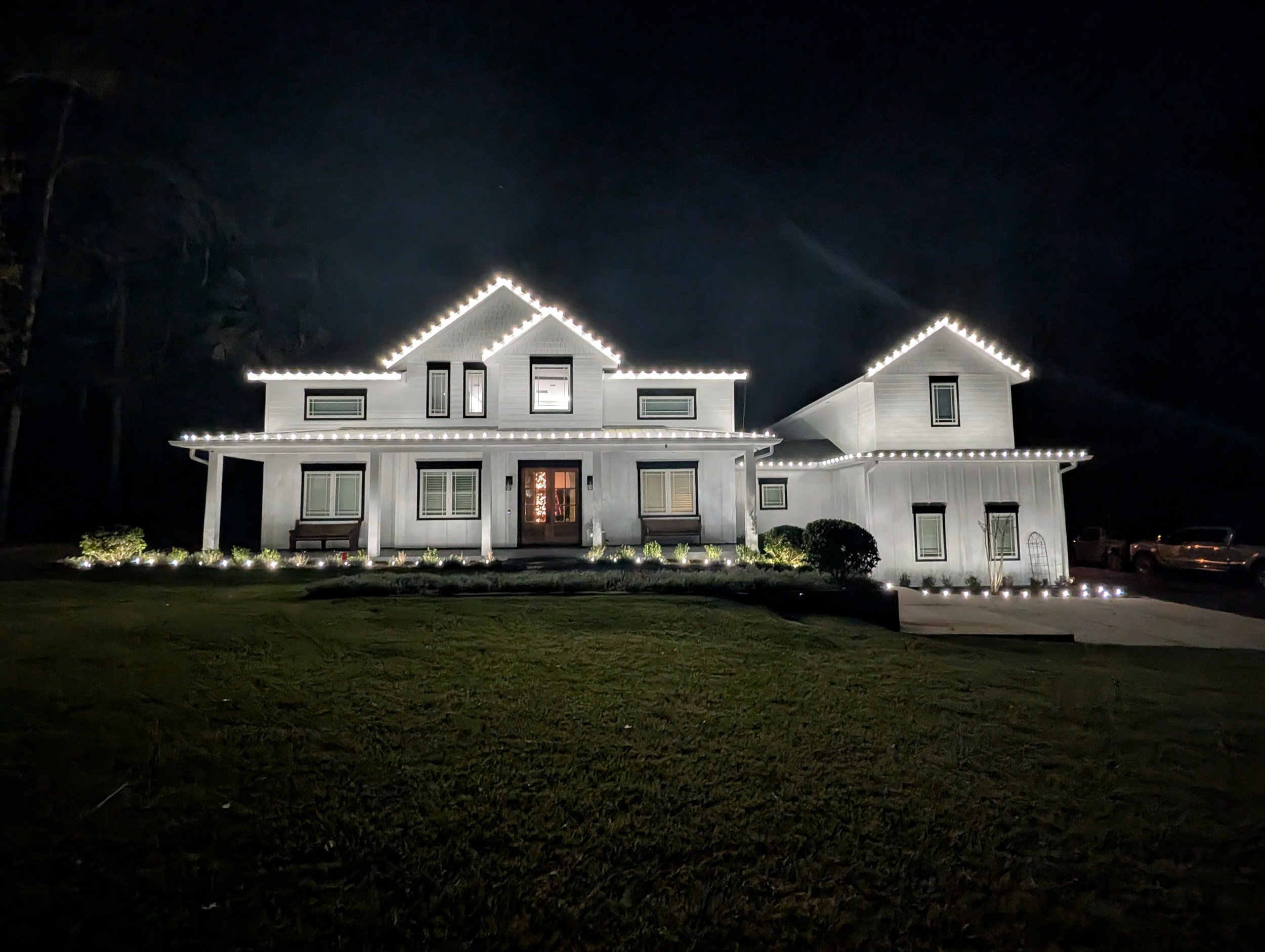 White farmhouse with illuminated roofline, porch and garden edge